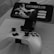 A mobile phone is mounted on a stand displaying a game titled 'Grimvalor' with options such as 'Continue', 'New Game', and 'Extras'. In front of the phone, there is a game controller placed on a table. The setup indicates gaming activity possibly using a smartphone as the screen.